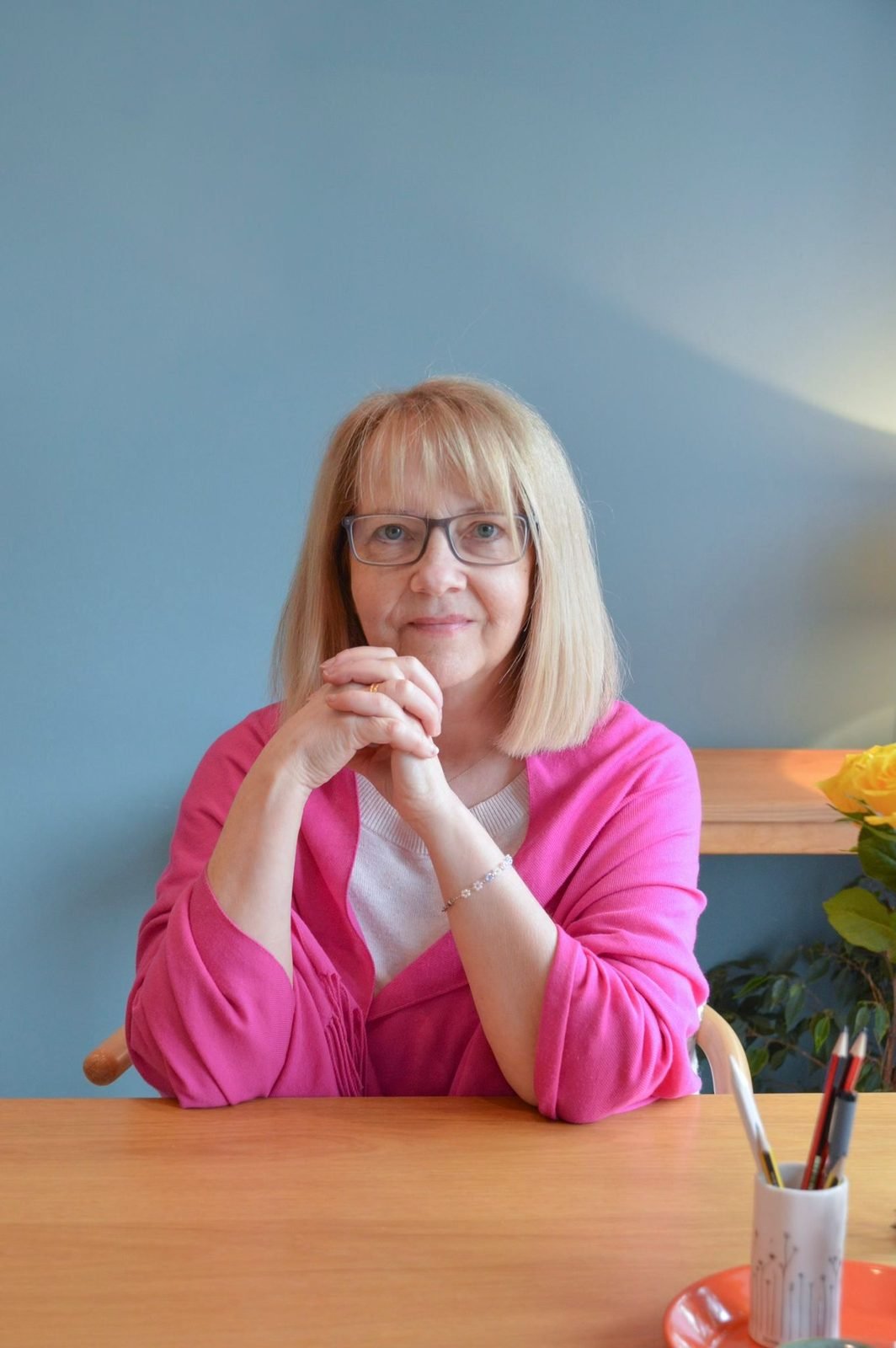 Christine, in a pink cardigan, seated at her desk with her hands clasped
