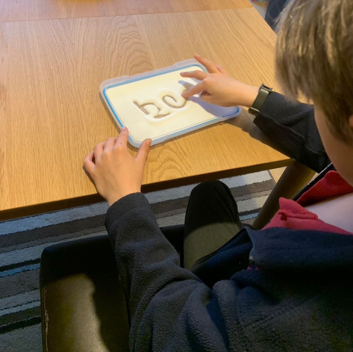 A child practising letters by writing them in a tray of salt, a multisensory technique